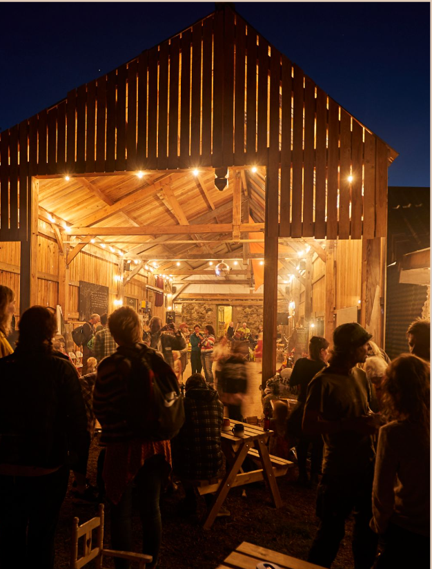 Cabaña de madera grande iluminada con gente unida en comida comunitaria